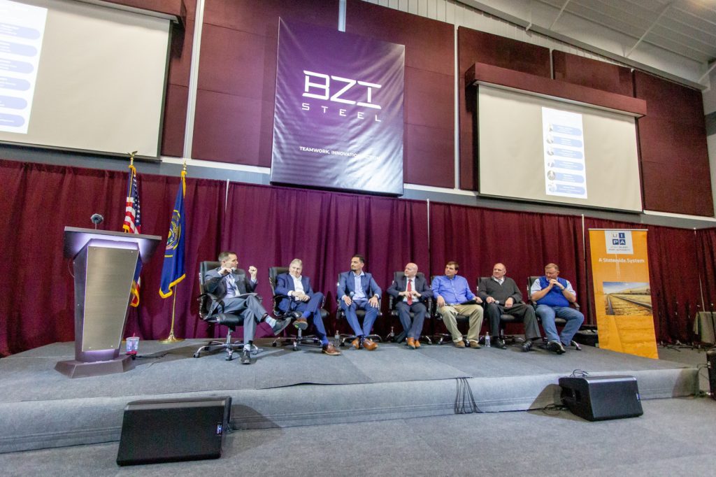 Panel of people sitting on raised platform in front of a maroon curtain