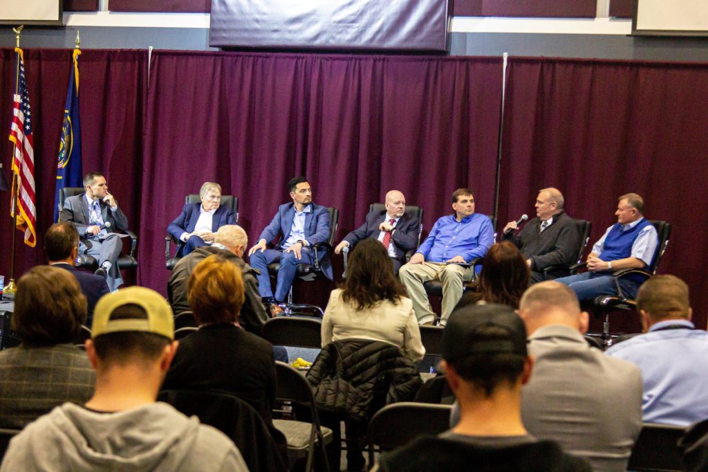 Panel of people sitting on raised platform in front of a maroon curtain